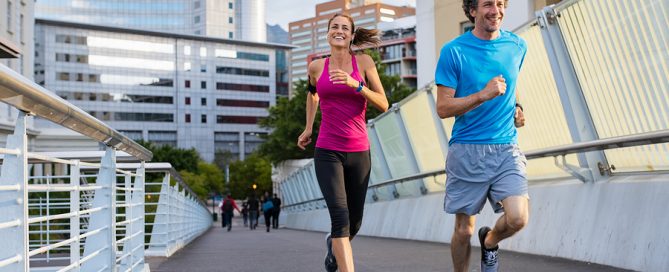 Happy man and beautiful woman jogging together city bridge. Healthy couple running on the city street. Middle aged couple running with building in the background.