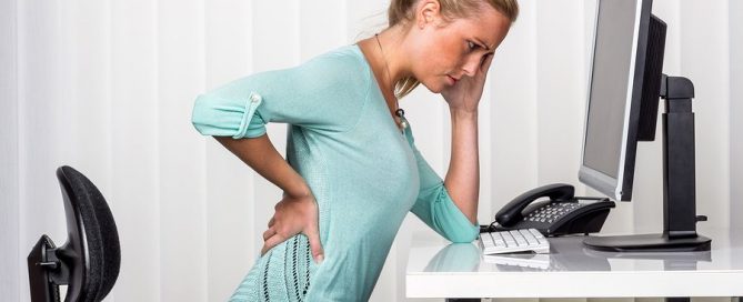 A woman sitting at a desk and experiencing back pain